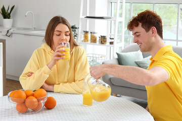 Canvas Print - Young couple drinking orange juice in kitchen