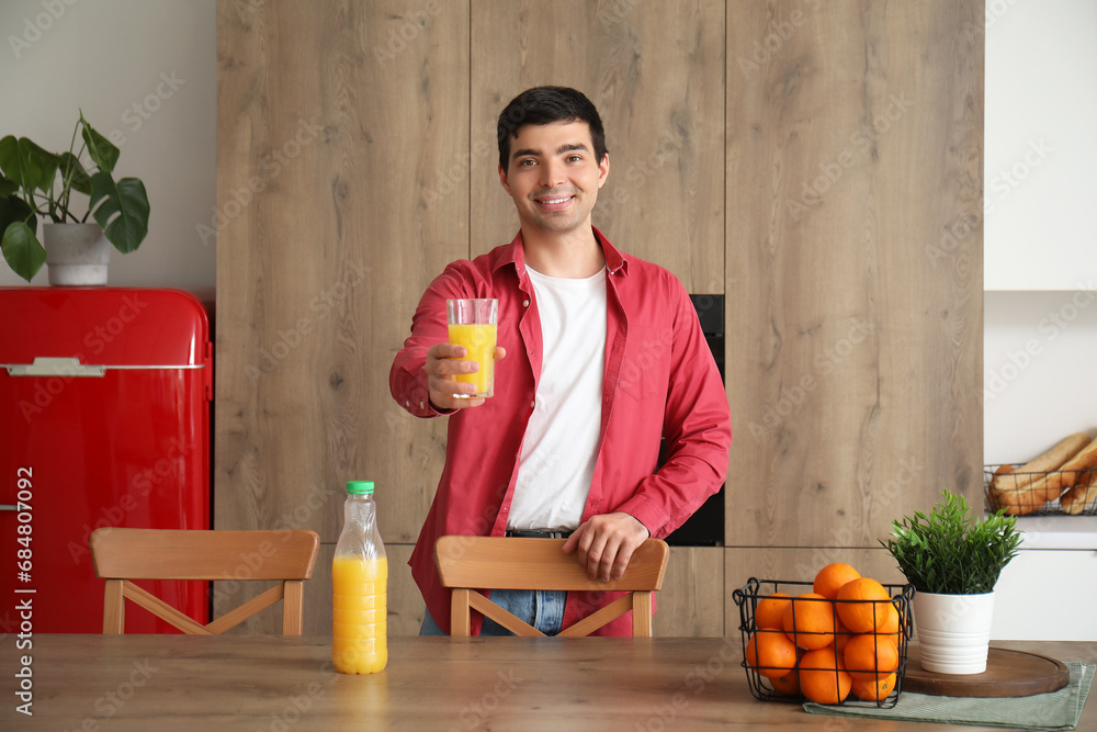Young man with glass of orange juice in kitchen