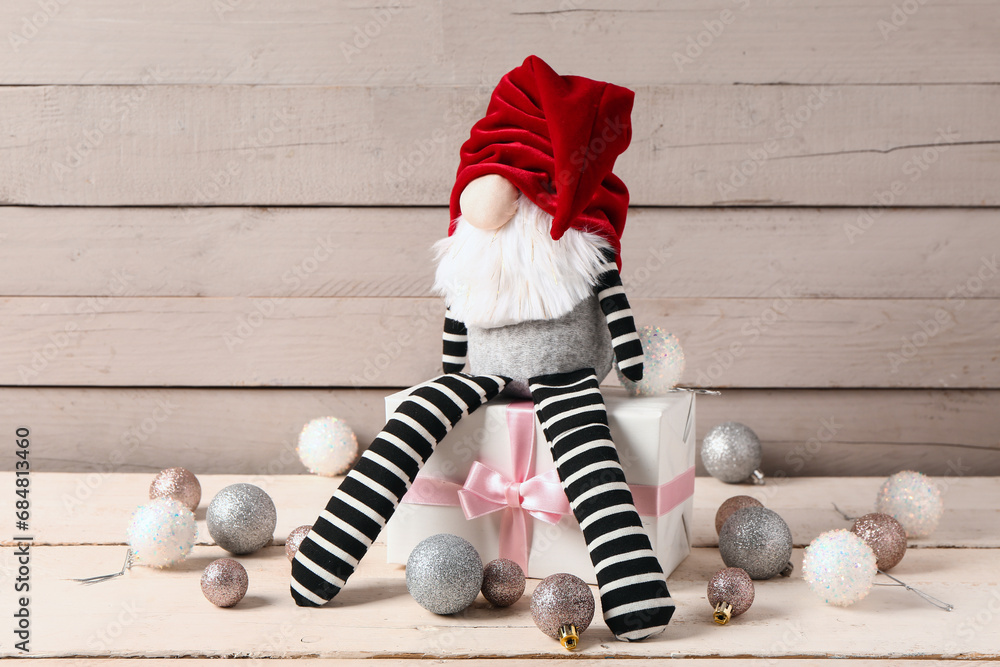 Christmas gnome with gift box and balls on white wooden background