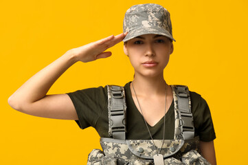 Wall Mural - Confident young female soldier in uniform saluting on yellow background