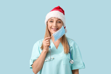 Canvas Print - Mature female doctor in Santa hat and medical mask on blue background