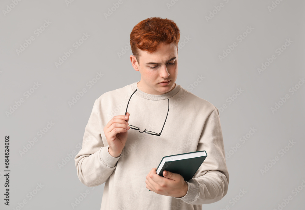 Young man with eyeglasses and book on grey background