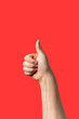 © pablo - Close-up of a male arm doing thumb up sign isolated on red background