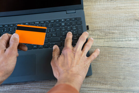 hand typing on a laptop, holding the orange credit card for online shopping, increase in online scams