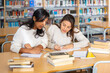 © JackF - Two hispanic women engaged in research, looking together for information in books in public library