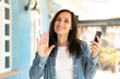 Middle aged woman using mobile phone at outdoors saluting with hand with happy expression