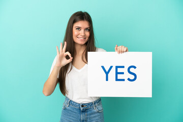 Wall Mural - Young caucasian woman isolated on blue background holding a placard with text YES