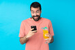 © luismolinero - Young man over holding a cocktail over isolated blue background surprised and sending a message