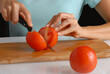 Woman slicing fresh tomato on kitchen board.