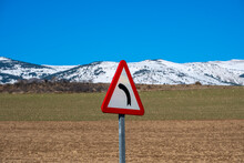 Traffic Sign With An Arrow Indicating A Curve In An Agricultural Landscape With The Snow-capped Pyrenees In Autumn In The Province Of Girona In Spain