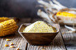 Corn flour or polenta wholemeal in a wooden bowl, maize cobs over old wooden background