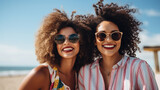 Two Afro American best female friends sitting together on beach smiling in the summer. Ethnic diverse friends hugging laughing and having fun