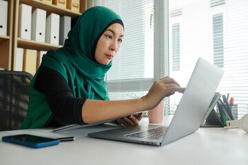 Wall Mural - Muslim businesswoman in hijab working on laptop at office desk