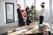 © sofiko14 - Attractive Caucasian businessman employee in suit and santa hat sitting at desk using laptop in christmas decorated office. Young corporate worker in festive workplace looking at screen of computer.