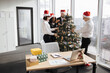 © sofiko14 - Multicultural team of business people celebrating new year in office with panoramic windows, decorating Christmas tree together, preparing for holiday party.
