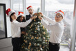 © sofiko14 - Multiethnic team of people putting christmas tree decor in festive office, preparing for winter season tradition at job. Decorating workplace with xmas ornaments for seasonal holiday.