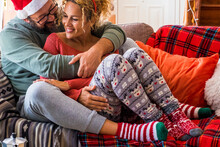 Couple In Love Enjoy Romantic Leisure Activity During Christmas Holiday Celebration Season. Man Hugging Woman  Both Sitting On The Sofa. Happy Wife And Husband With Xmas Decorations At Home. Relax