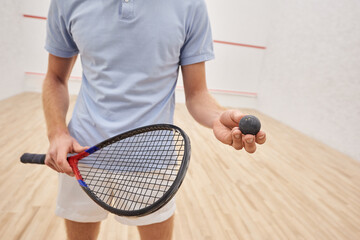 Wall Mural - cropped view of man in sportswear holding squash ball and racquet and standing inside of court