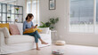 © ChayTee - Internet of things smart tech urban house IOT appliances better life. Asia Gen Z people young woman easy relax neat chores enjoy home care to robot hoover clean floor mobile app at sofa living room.