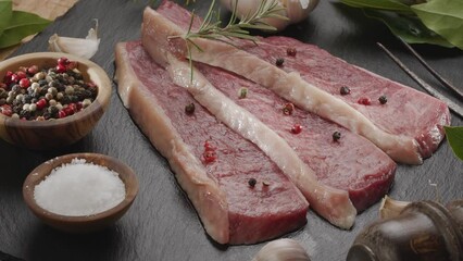 Poster - Three sliced pieces of picanha beef with spices and herbs on a gray stone countertop slowly rotate in the frame. Traditional Portuguese food.