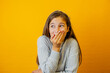 Little cute girl joyfully surprised holds her hands near her mouth and shows with her hand on isolated yellow background