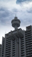 Wall Mural - Brutalist architecture. A tall concrete residential estate with a tower on top of it's side and a grey cloudy sky in the background. Photorealistic 3D illustration.