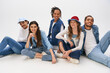 © LIGHTFIELD STUDIOS - stylish multiethnic friends in casual street wear sitting and smiling at camera on grey backdrop
