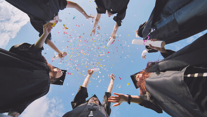 Wall Mural - Happy graduates throwing up colorful confetti against the blue summer sky.