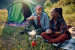 Happy multiracial couple having cup of warm tea while camping in nature.
