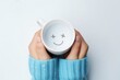 A person holding a cup with a smiley face drawn on it. This versatile image can be used to represent happiness, positivity, or even the simple joy of enjoying a warm beverage