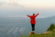 © narong - Wide shot of back of woman wear red coat and stand with spread her arms near cliff on the mountain and look forward to beautiful view with warm light of sun rising.