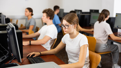 Wall Mural - Interested young female student with glasses working on computer in university library, looking for necessary information on Internet