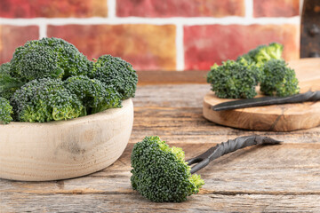 Wall Mural - Raw broccoli florets in wooden bowl.  Single floret on a fork laying on a table.