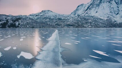 Wall Mural - Aerial view from low flying drone of frozen lake in snowy mountains in winter at sunrise. Lofoten islands, Norway. Top view of frosted river, reflection on ice, snowy rocks, purple sky. Cloudy weather