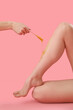 Hand applying sugaring paste onto young woman's legs against pink background