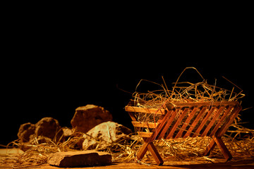 Manger with hay and stones on wooden table against dark background