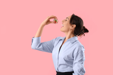 Canvas Print - Happy young woman eating tasty maki roll on pink background