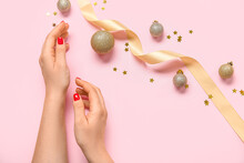 Female Hands With Red Manicure, Golden Christmas Balls And Ribbon On Pink Background