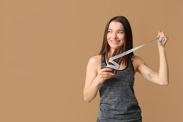 Canvas Print - Young woman with chocolate bar and tape measure on brown background