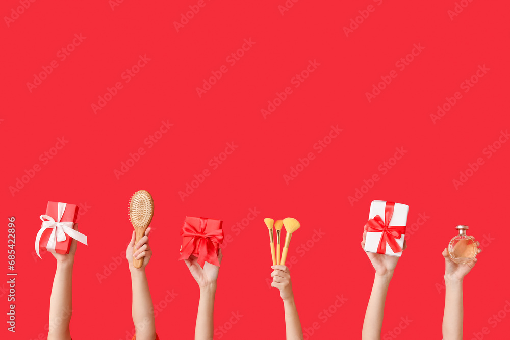 Female hands with different cosmetic items and gifts on red background