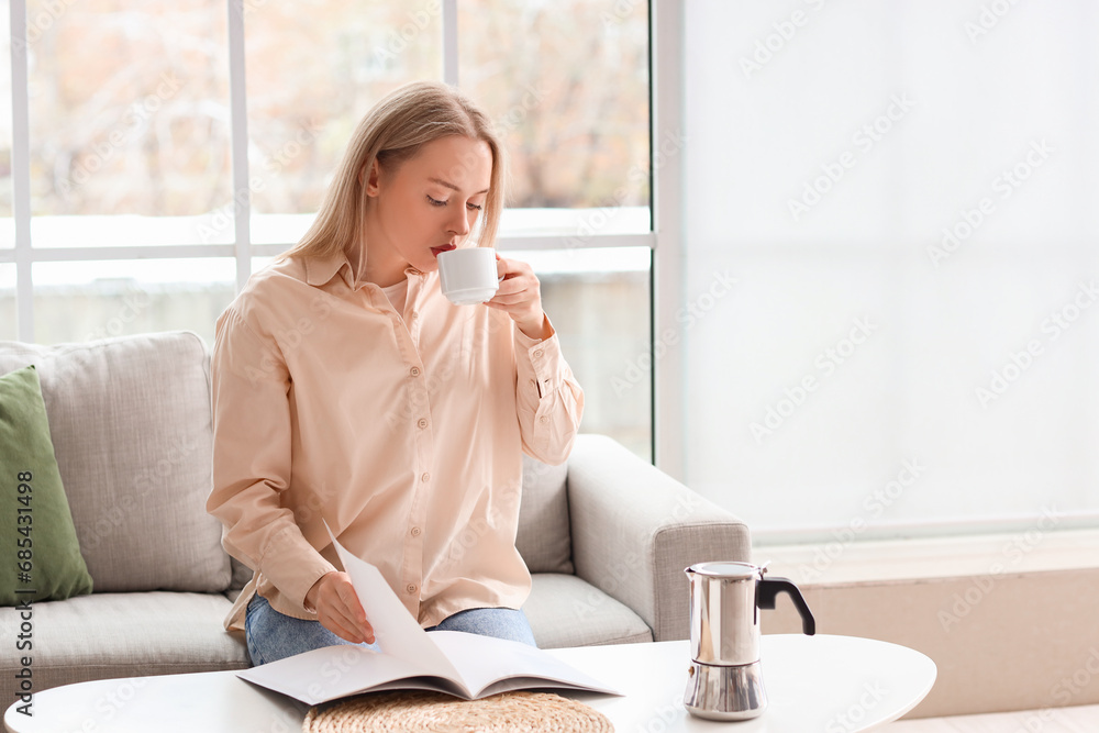 Pretty young woman reading magazine while drinking coffee in living room