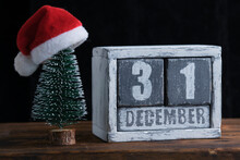 December 31 On Wooden Calendar Standing Next To Christmas Tree Decorated With Santa Claus Hat.