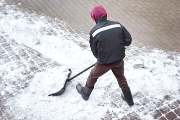 Wall Mural - Snow removal work, clean snowy walkway. Worker in action shoveling snow from sidewalk, MOTION BLUR. Man clearing snow from path with shovel, aerial view. Utility man with spade cleans snowy street