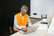 senior mature man engineer with laptop computer typing on laptop wear safety vest. Work housing projects and architecture