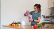 © Natee Meepian - Beauty healthy asian woman making fruit smoothie with blender. woman drinking glass of fruit smoothie in kitchen. Diet concept. healthy drink