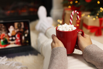 Wall Mural - Woman drinking delicious cocoa and watching Christmas movie at home, closeup. Space for text