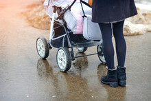 Trendy Woman With Baby Carriage Walk On Wet Sidewalk In The City In Winter Season. Fashionable Woman Push Baby Stroller, Walking On Wet Asphalt. Selective Focus