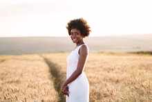 Happy Young Woman Standing In Wheat Field At Sunset