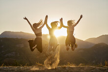 Cheerful Friends Holding Hands And Jumping At Sunset