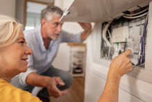 Woman Examining Electrical Cable In Fuse Box With Man At Home
